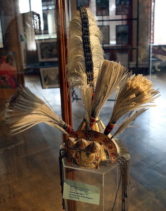 Couronne d'argent ornée de plumes blanches, présentée sous vitrine avec l'étiquette « Heritage from Kaffa Kingdom »