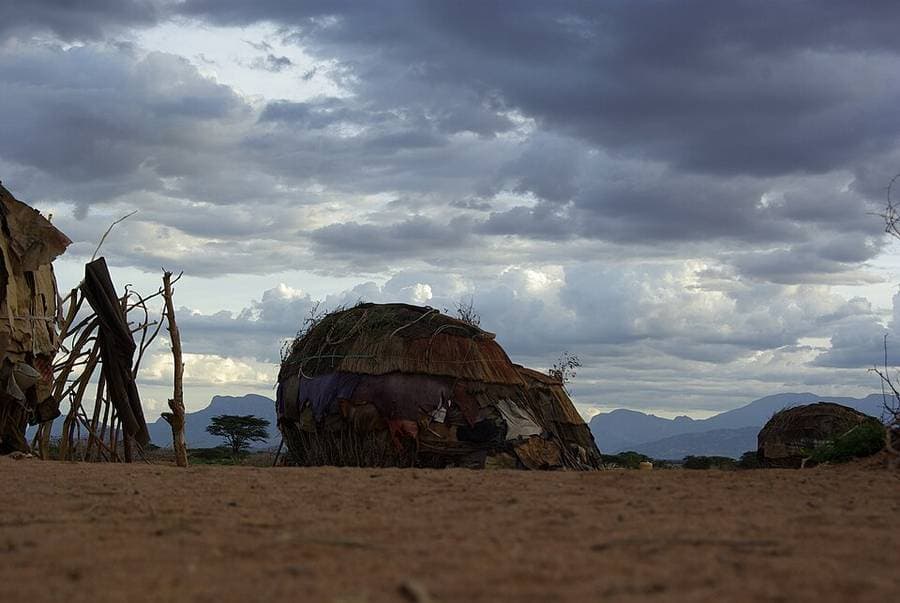Une maison rendille en dôme, couverte de nattes, de peaux et de pièces de tissu, sous un ciel d'orage au nord du Kenya