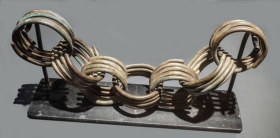 Anneaux de métal cuivreux enroulés et entrelacés, présentés sur un socle de musée