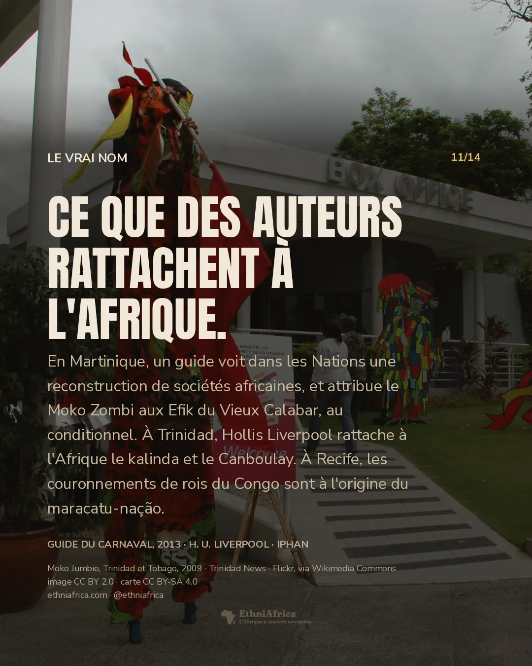 Deux échassiers en costume, l'un en orange à motifs de têtes de mort, l'autre en violet, tenant chacun un drapeau rouge, devant un bâtiment blanc portant l'enseigne « Box Office » et deux silhouettes découpées de personnages de carnaval sur une pelouse.