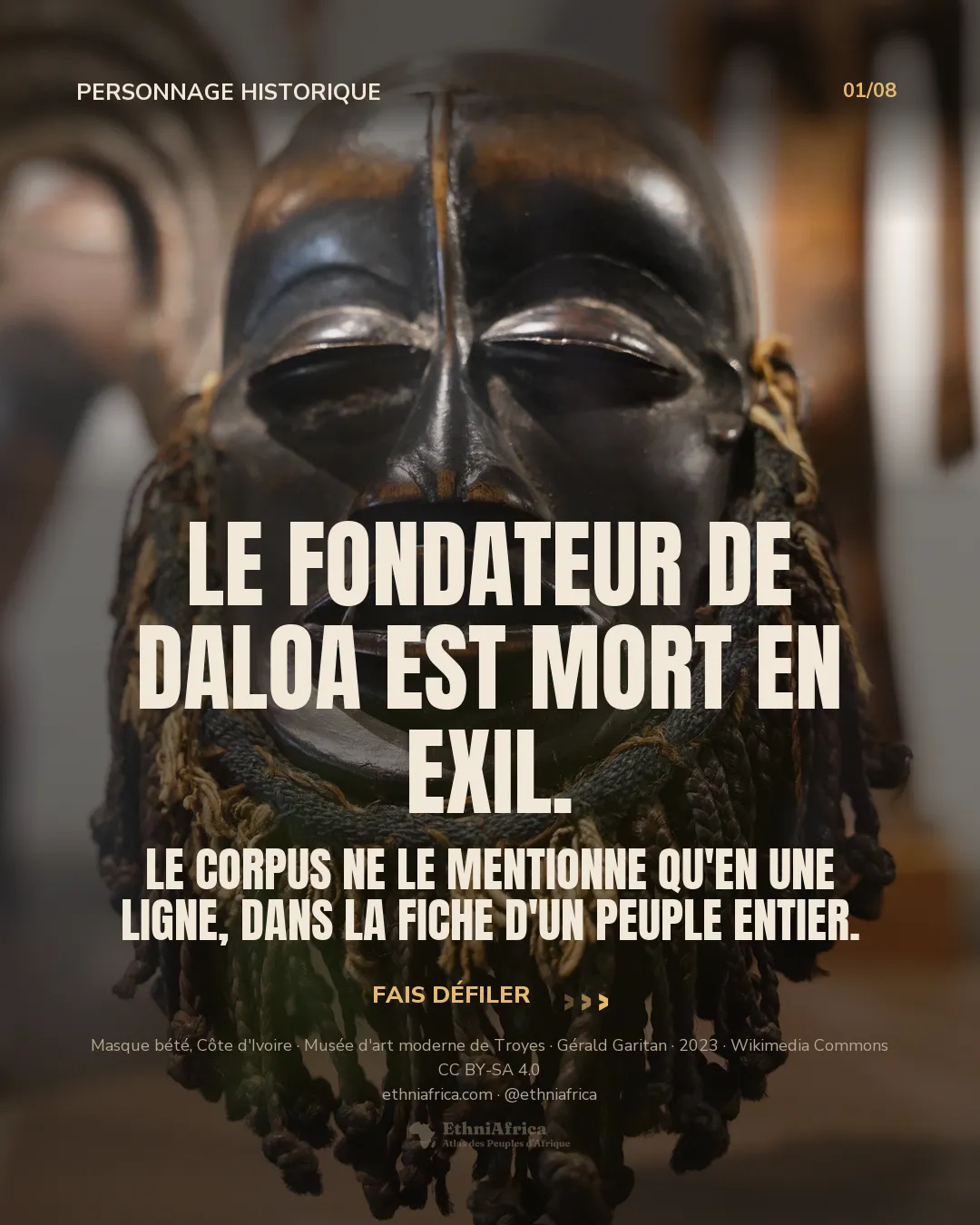 un masque bété en bois sombre poli, visage lisse aux yeux mi-clos, une barbe de cordelettes tressées vertes et beiges suspendue sous le menton, exposé en musée, d'autres masques flous à l'arrière-plan