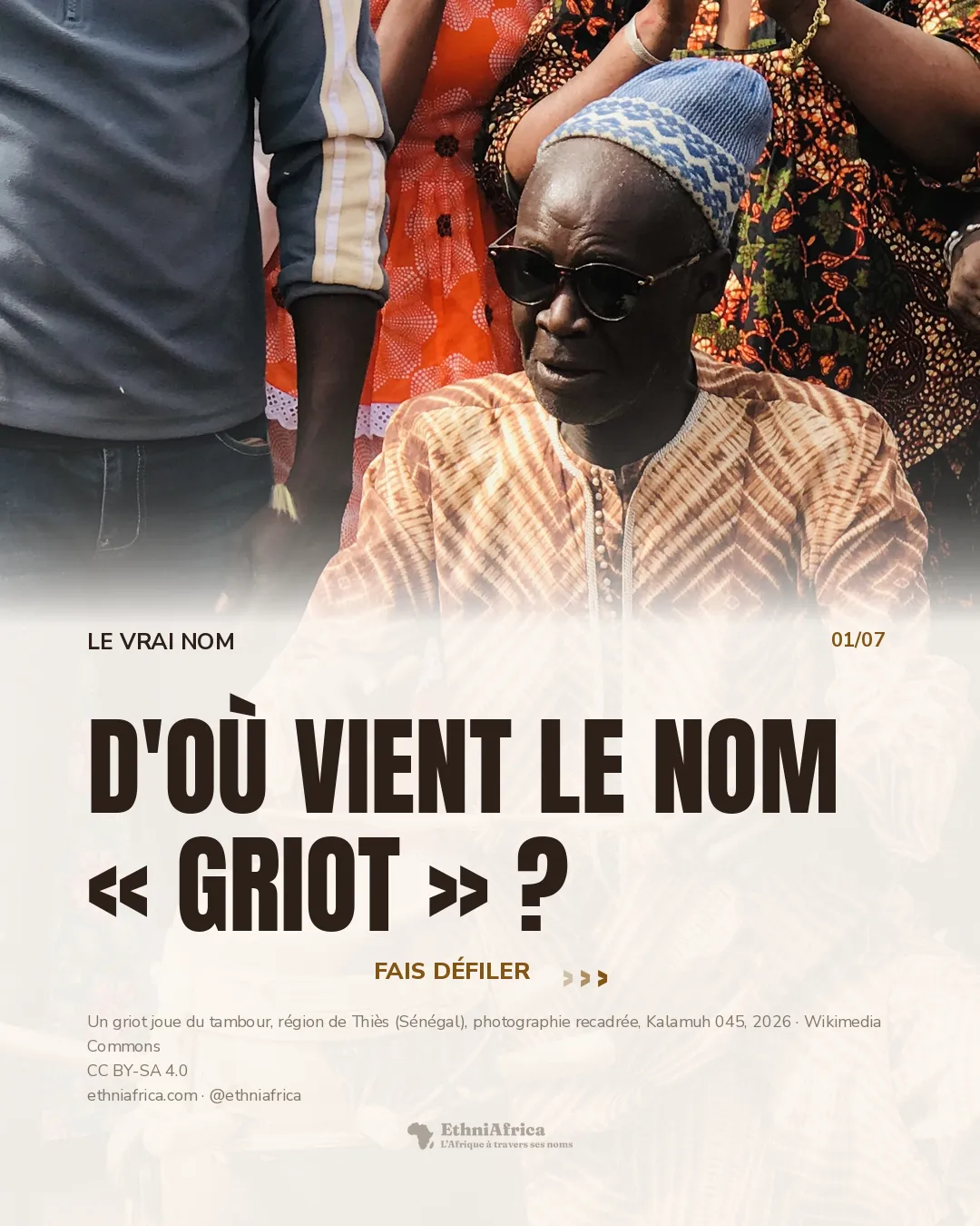 un griot âgé, lunettes noires et bonnet brodé, frappe un grand tambour avec une baguette ; derrière lui, des vêtements et des mains qui applaudissent