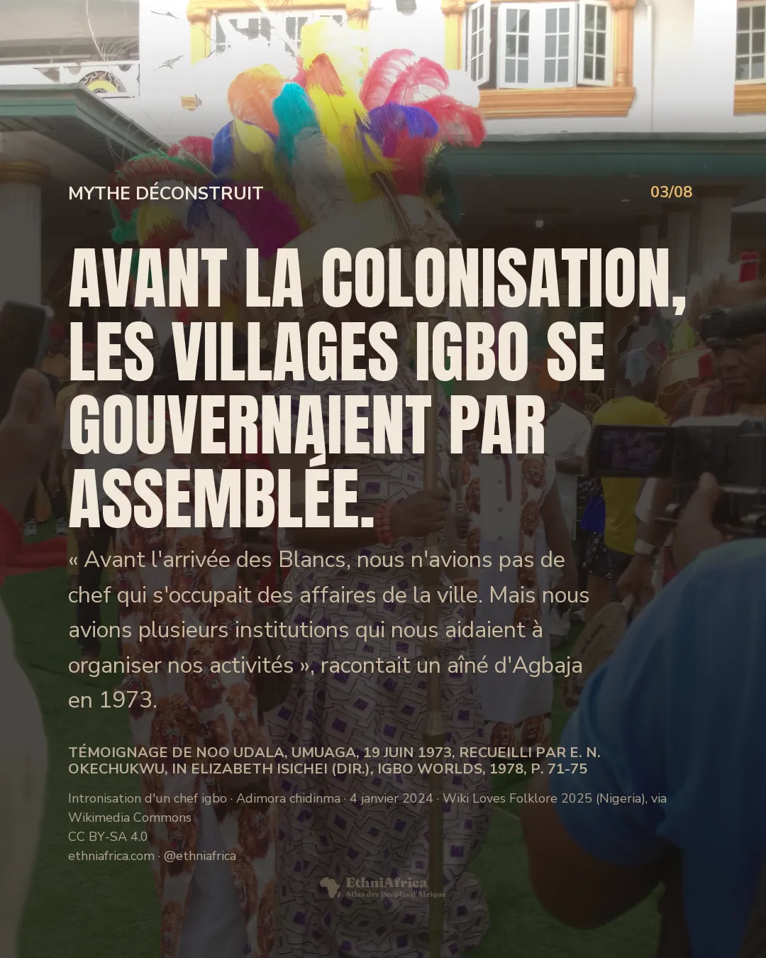 un chef vêtu d'une tenue cérémonielle à motifs pourpres et dorés, coiffé d'une haute coiffe à plumes multicolores, tenant un bâton doré, entouré de dignitaires et de photographes lors d'une cérémonie d'intronisation