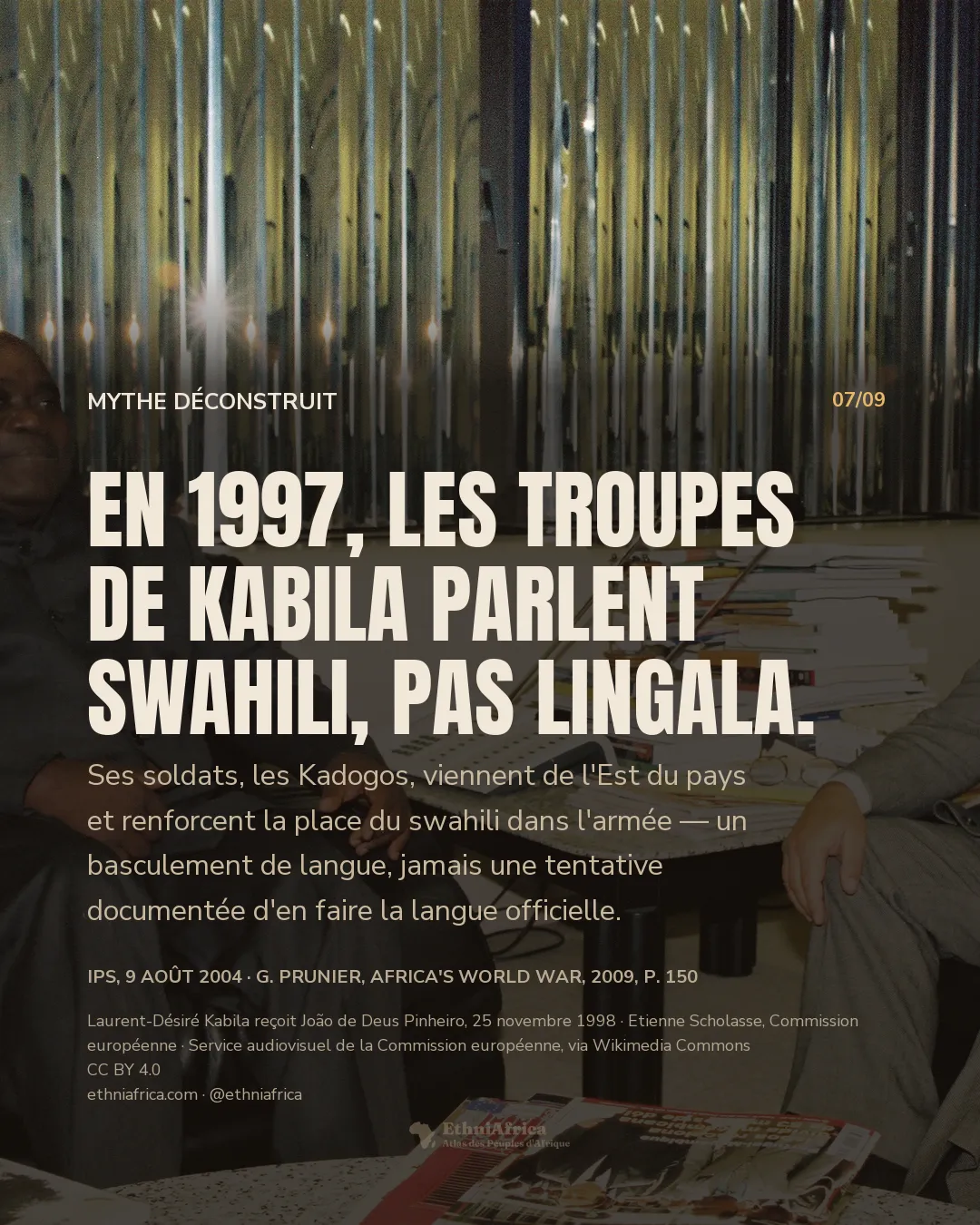 Deux hommes assis dans des fauteuils de cuir, en pleine conversation souriante, autour d'une table basse couverte de livres et d'un téléphone, dans un bureau aux parois métalliques verticales.